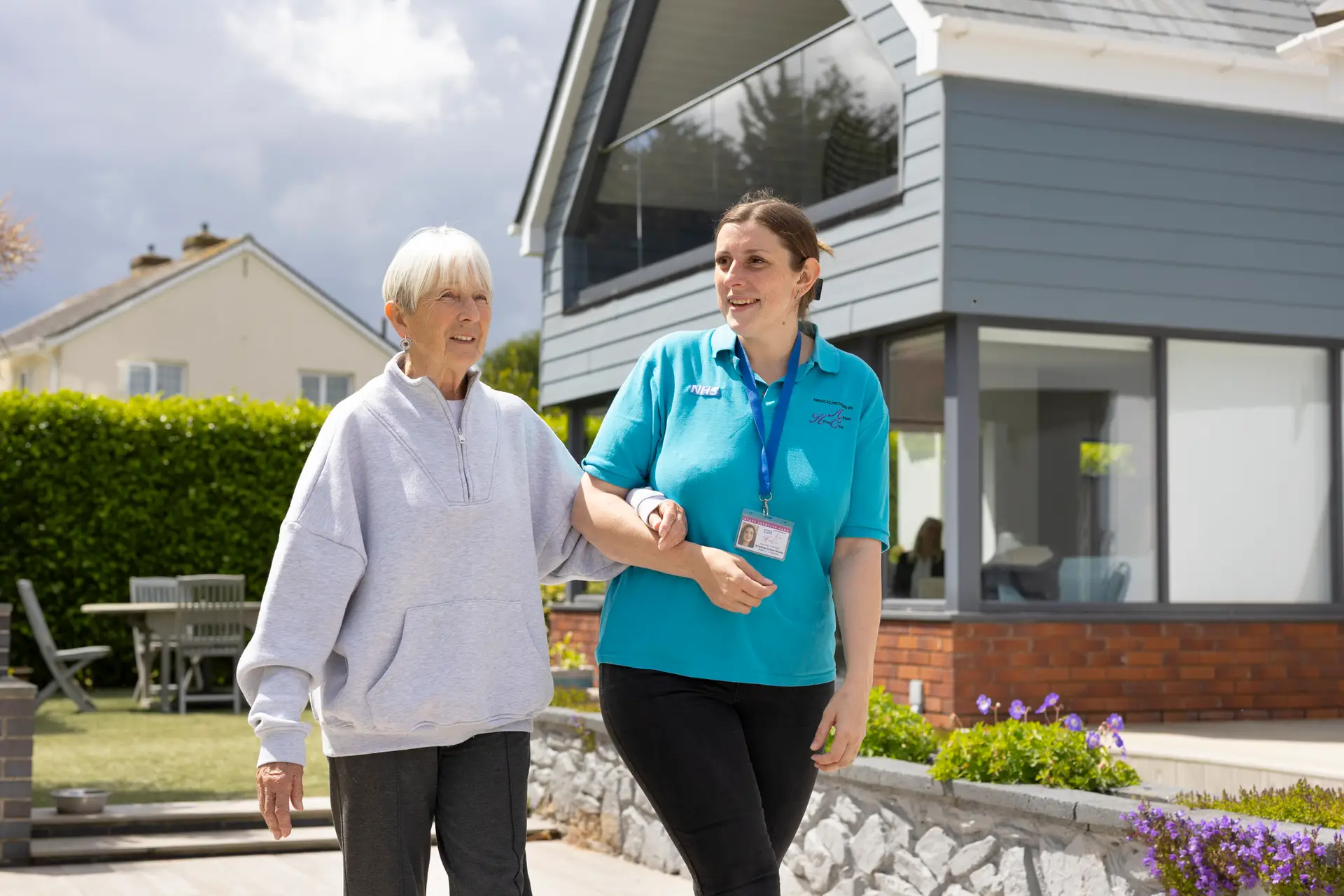 Care worker walking arm in arm with an elderly woman outdoors.