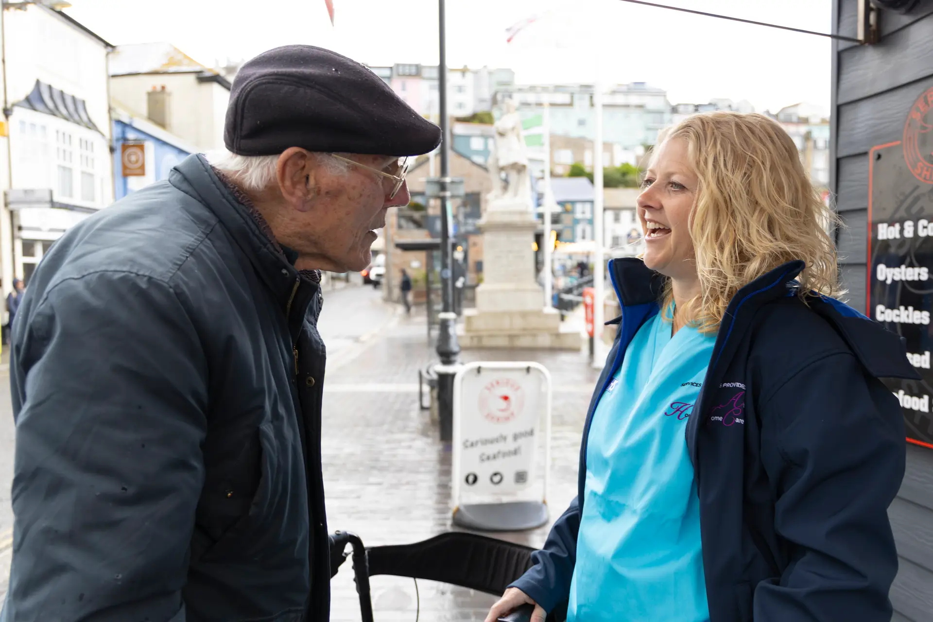 Care worker chatting happily with an elderly man during an outdoor outing in town.
