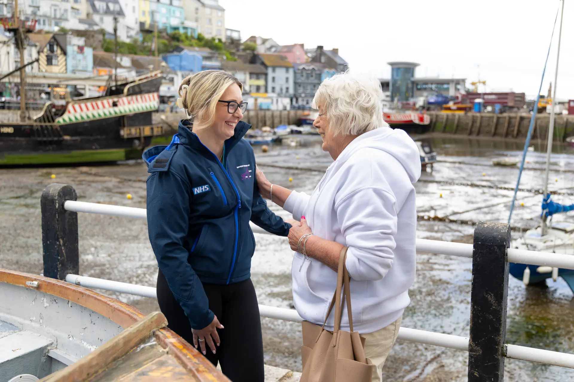 Care worker talking with an elderly woman by a harbour.
