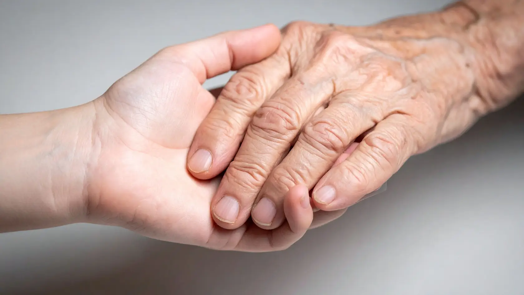 Close-up of well-groomed, healthy nails on an elderly person's hand resting in a caregiver's hand.