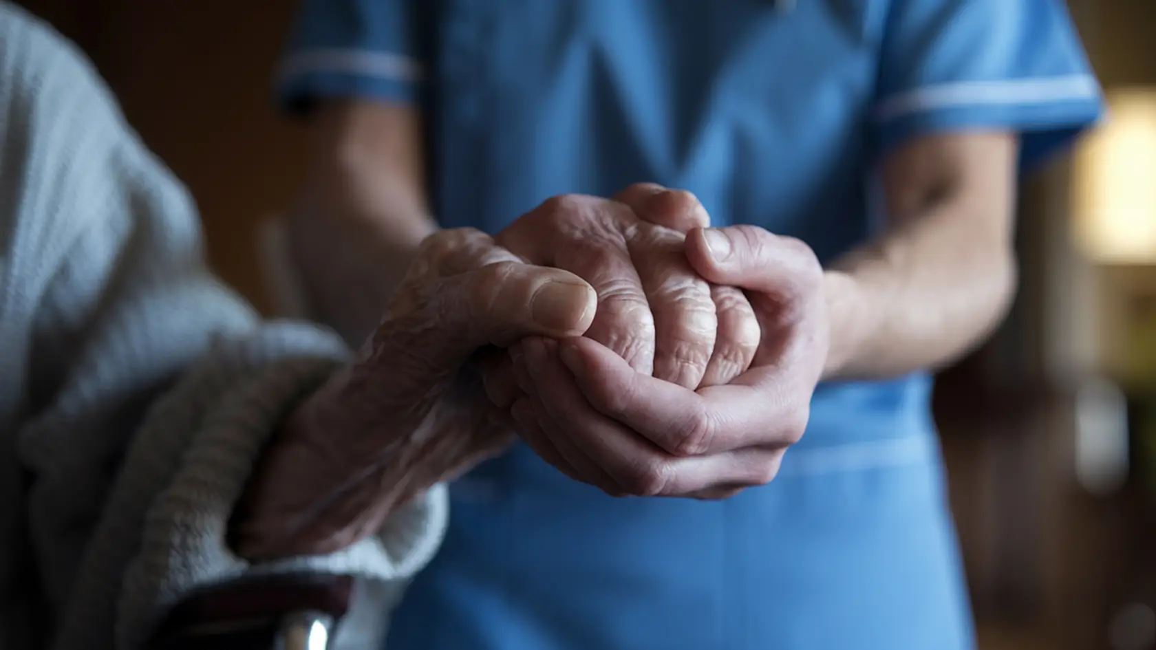 Abide care worker gently holding the hands of an elderly person.